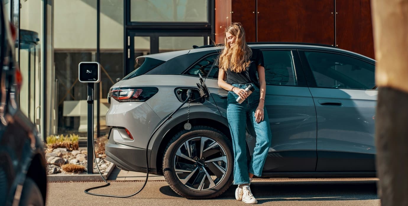 Femme adossée à son véhicule électrique en cours de charge